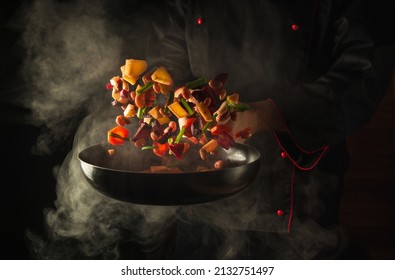 Chef prepares food in a hot pan with steam on a black background. The concept of restaurant and hotel service. Haute cuisine or Grande cuisine - Shutterstock ID 2132751497