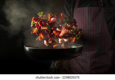 Chef prepares food in a hot pan with steam on a black background. The concept of restaurant and hotel service. Grande cuisine - Shutterstock ID 2198035575