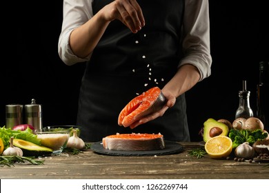 The Chef Prepares Fresh Salmon Fish, Smorgu Trout, Sprinkling Salt With The Ingredients. Frost Freezing In The Air. Preparing To Cook Fish Food. Salmon Steak. Woman Cook