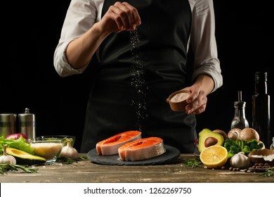 The Chef Prepares Fresh Salmon Fish, Smorgu Trout, Sprinkling Salt With The Ingredients. Frost Freezing In The Air. Preparing To Cook Fish Food. Salmon Steak. Woman Cook