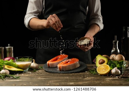 The chef prepares fresh salmon fish, smorgu trout, sprinkling salt with the ingredients. Frost freezing in the air. Preparing to cook fish food. Salmon steak. Woman cook