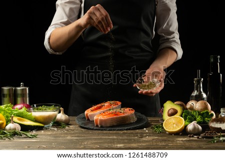 The chef prepares fresh salmon fish, fresh salmon, sprinkles with spices and Provencal herbs with ingredients.Frost in the air. cooking fish food.Cooking vegan cuisine, restaurants,hotel business