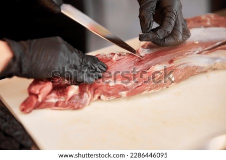 A chef prepares a large piece of fresh raw meat lying on a cutting board in a commercial kitchen. a large piece of raw veal lies on a plastic cutting board. juicy large piece of raw veal
