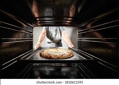 Chef prepares pizza in the oven, view from the inside of the oven
