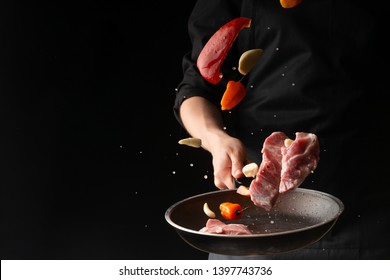 The chef prepares steaks from meat, pork or beef, throwing fresh meat with sweet peppers and garlic on a black background in a skillet, horizontal photo, menu, recipe book, restaurants - Powered by Shutterstock