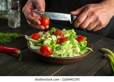 Chef prepares a vegetable salad in the kitchen table. Cutting a fresh tomato for a vitamin salad with a knife - Powered by Shutterstock