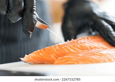 Chef preparing a fresh salmon fillet in Japanese kitchen. Close up hand of chef Pulling salmon fish bone for making sashimi. - Powered by Shutterstock