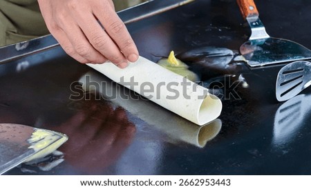A chef is preparing kebabs on a hot, buttered pan using a spatula and tongs, ready to be served to customers.