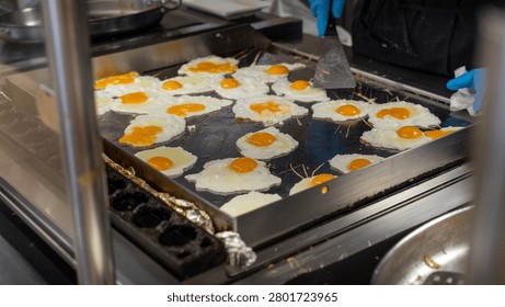 Chef preparing multiple sunny side up eggs on a large commercial griddle in a restaurant kitchen, breakfast food production and catering service.