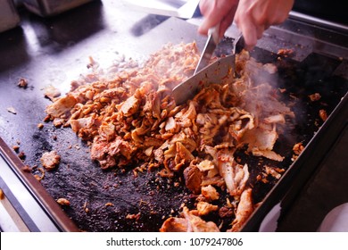 Chef preparing some Mexican tacos al pastor on a hot griddle.