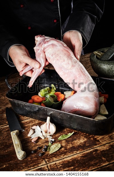 Chef preparing wild rabbit\
for roasting in a rustic kitchen displaying the cleaned skinned\
carcass to the view in a roasting pan with diced vegetables and\
seasoning