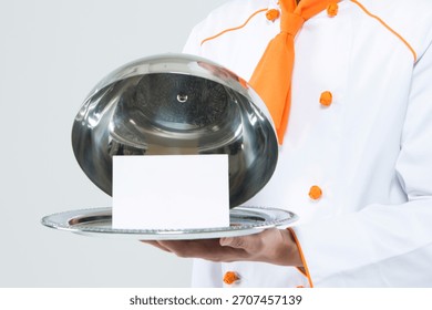 Chef presenting a covered dish with an empty card in a modern kitchen setting