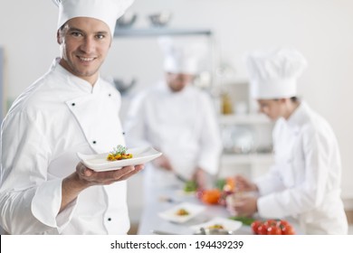 Chef Presenting A Dish With His Team In Background