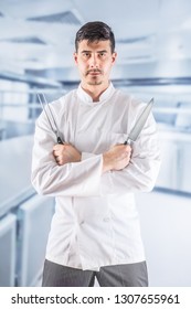 Chef professional in restaurant kitchen standing with crossed hands and holding fork and knife.