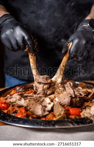 Chef pulling tender roasted lamb leg by hand over baked vegetables on a large platter highlighting halal friendly festive cuisine and rich traditional flavors