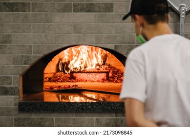 The chef puts the Margherita, four cheese or meat pizza on a shovel in the oven. A firewood oven for cooking and baking pizza. Italian traditional pizza is cooked in a stone wood-fired oven. Back view - Shutterstock ID 2173098845