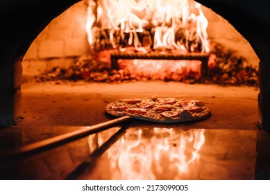 The chef puts the Margherita, four cheese or meat pizza on a shovel in the oven. A firewood oven for cooking and baking pizza. Italian traditional pizza is cooked in a stone wood-fired oven. - Powered by Shutterstock