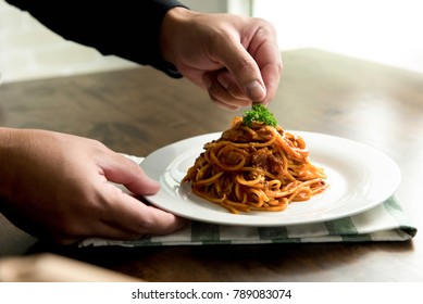 Chef putting parsley on top of delicious spaghetti bolognese in a white plate on kitchen table - Powered by Shutterstock