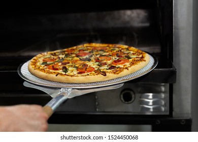 Chef putting pizza baking sheet in oven at restaurant with pizza shovel.