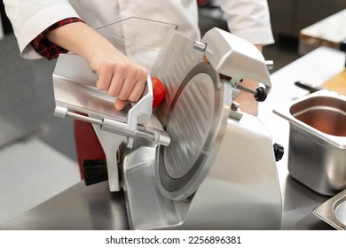 The chef in the restaurant kitchen prepares tomato slices with a slicer - Powered by Shutterstock