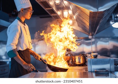 Chef in restaurant kitchen at stove and pan cooking flambe on food - Powered by Shutterstock