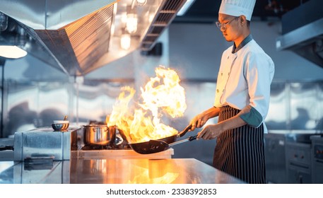 Chef in restaurant kitchen at stove and pan cooking flambe on food - Powered by Shutterstock