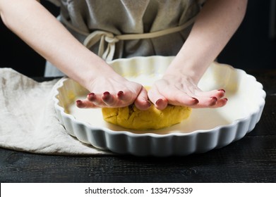Chef rolls out the dough in a baking dish, cooking. Side view, black background, close up