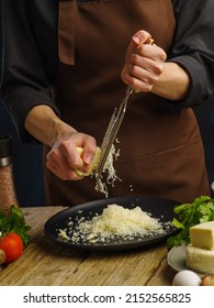 The chef rubs the cheese on a manual grater. Ingredients for cooking salad, pizza, pasta, spaghetti, lasagne. Restaurant, hotel, cafe, home cooking. Recipes for dishes with grated cheese.
