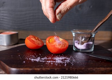Chef salting a halved tomato on a wood cutting board