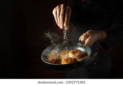The chef salts hot pancakes in a frying pan while frying. Concept of cooking blini in a restaurant kitchen. Black space for advertising.