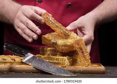 The chef serves bee honey in combs with his hands. Close up on a wooden table. Organic farm food concept.