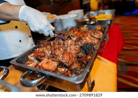 Chef serving roasted meat from a buffet tray with tongs during a catered event, showcasing freshly cooked food and warm dining ambiance.