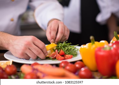 chef serving vegetable salad on plate in restaurant kitchen - Shutterstock ID 1083125597