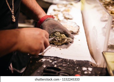Chef shucking a fresh oyster with knife and stainless steel mesh oyster glove.