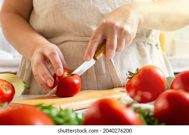 Chef slicing tomato using knife on the table in restaurant. Process of cutting and preparation food in kitchen.