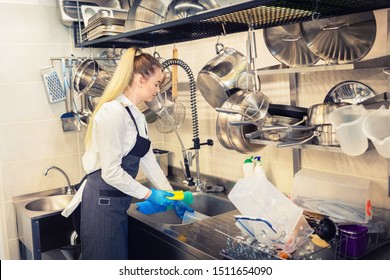 Chef of small restaurant washing dishes in sink at end of working day – kitchen worker using sponge to clean dishes – young woman at work in eatery kitchen - Powered by Shutterstock