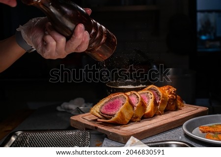 Chef spreading black pepper in beef Wellington platter at high cuisine restaurant's kitchen