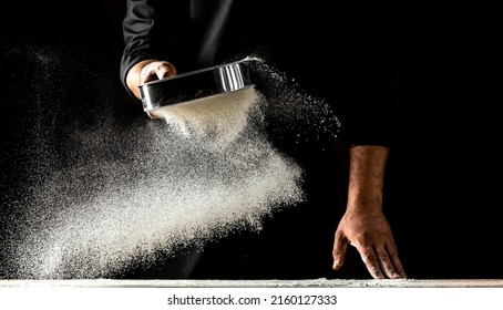 The Chef Sprinkles Flour Through A Sieve, Powdery Flour Flying Into Air. Chef Hands With Flour In A Freeze Motion Of A Cloud Of Flour Midair.