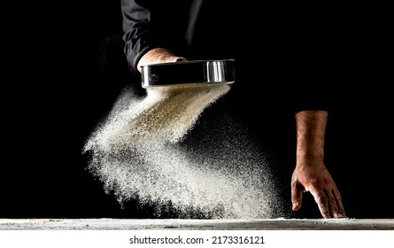 the chef sprinkles flour through a sieve, Powdery flour flying into air. chef hands with flour in a freeze motion of a cloud of flour midair.