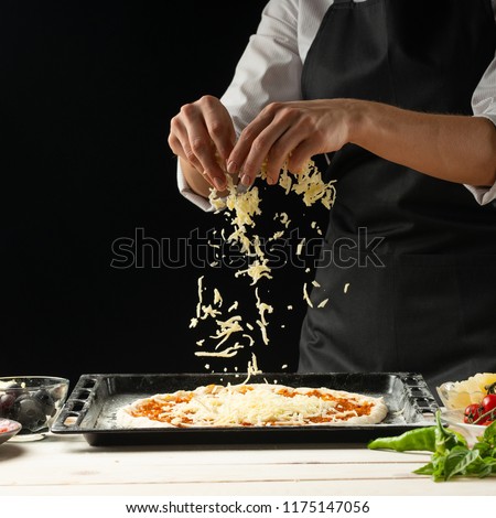 The chef sprinkles the pizza with cheese on a dark background, with free space