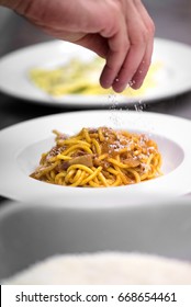 Chef Sprinkling Parmesan Cheese On A Plate Of Freshly Cooked Italian Pasta In A Close Up View Of The Food And His Hand