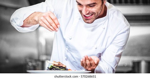 Chef sprinkling spices on dish in commercial kitchen