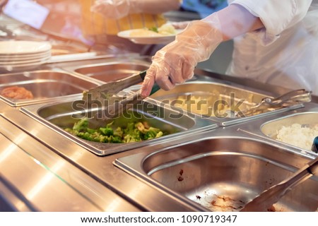 Chef standing behind full lunch service station with assortment of food in trays.