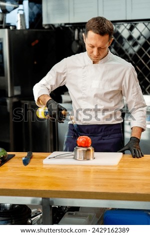 the chef is standing in the kitchen in a white jacket holding a torch and about to burn a tomato