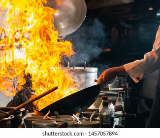 Chef Stir Fry In Wok. Dramatic Cooking With Fire Hard At Kitchen