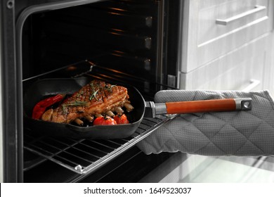 Chef taking pan with delicious roasted ribs out of oven, closeup