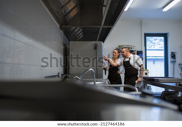 Chef teaching cook how to use combi oven indoors\
in restaurant kitchen.