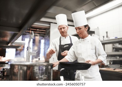 Chef, teamwork and kitchen or pan cooking for hospitality service as preparation, learning or catering. Man, woman and hat at stove for teaching skill for fine dining presentation, recipe or cuisine - Powered by Shutterstock