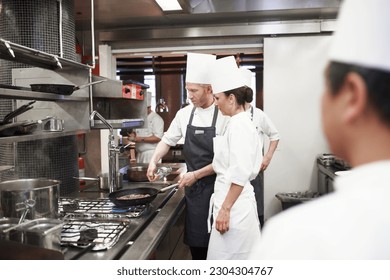 Chef, teamwork and people with frying pan in kitchen, catering service and prepare food for fine dining. Professional, cooking and man training woman, saute and cook add oil to meat in restaurant. - Powered by Shutterstock