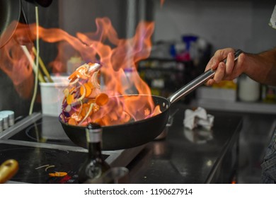 Chef Tossing Vegetables Flambe In A Pan Over The Burner